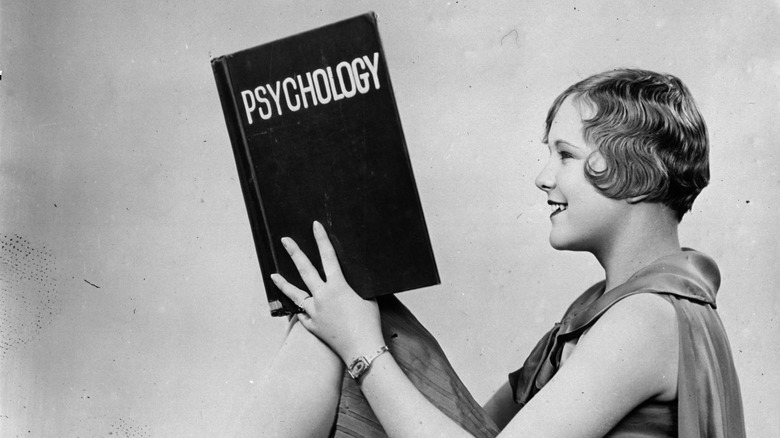 A black and white photo of a woman with 1920s hairstyle reading a Psychology book