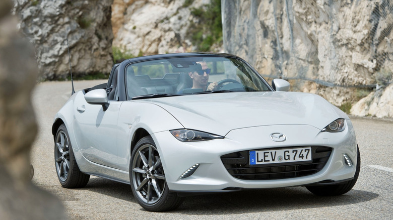 Mazda Miata convertible with the top down driving through rocky canyon roads