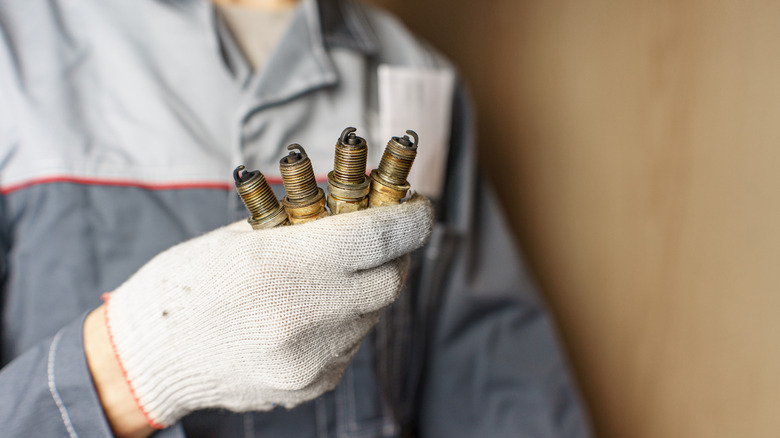 A mechanic holds four used spark plugs.