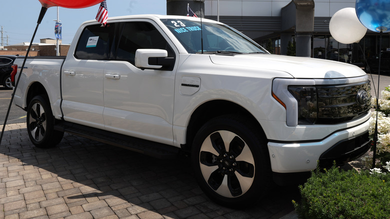 A white 2023 Ford F-150 Lightning EV is offered for sale at a dealership.
