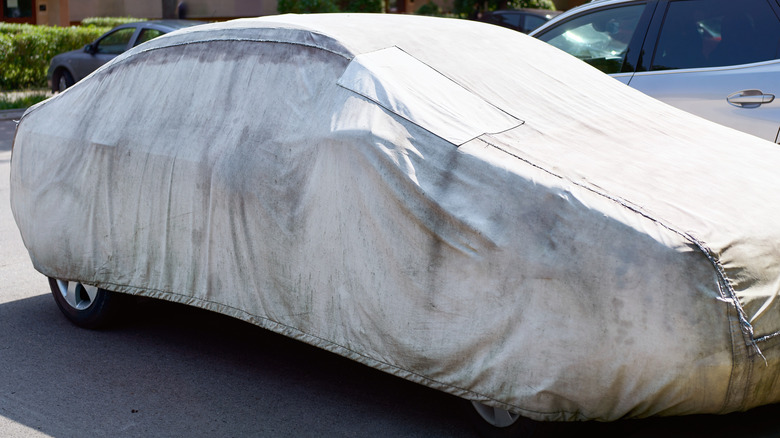 A car parked outdoors while draped in a dirty car cover