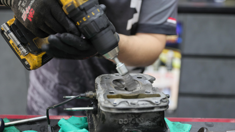 A person using a wire brush drill attachment to clean a cylinder head