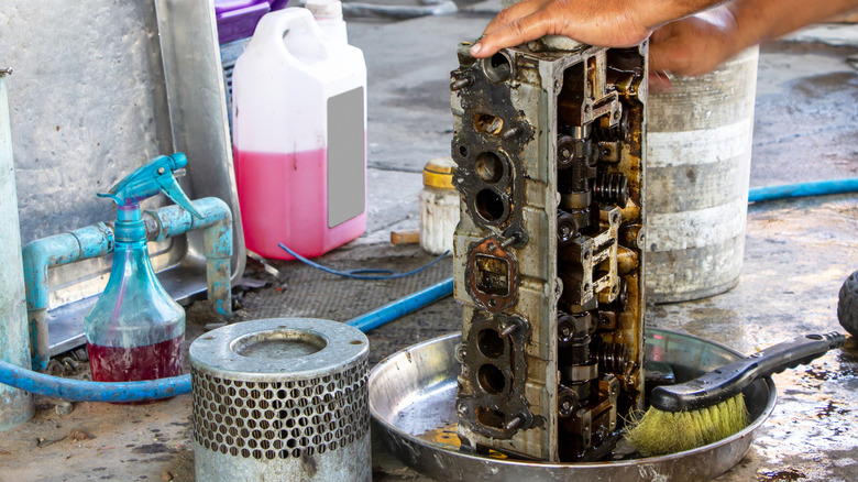 A person cleaning an engine cylinder head inside a container