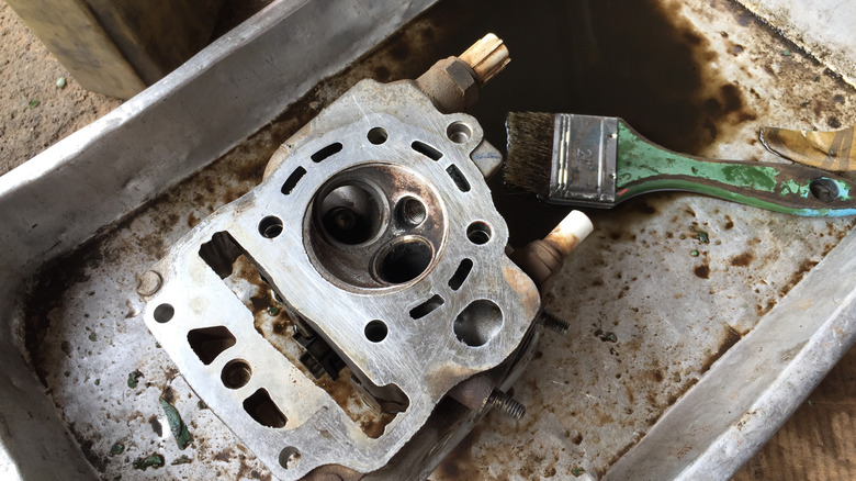 A close up of a torn-down motorcycle cylinder head with a green paintbrush