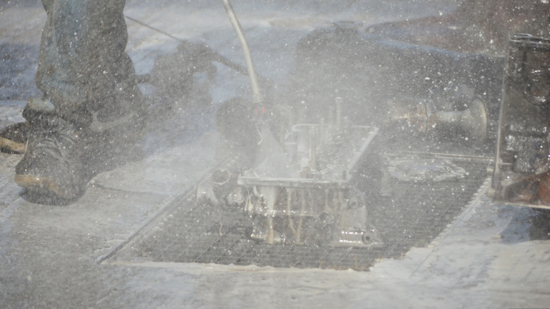 A person washing an engine cylinder head
