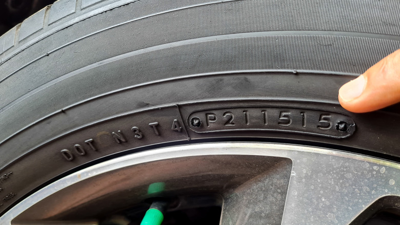 A finger points at the DOT tire codes on the sidewall of a tire