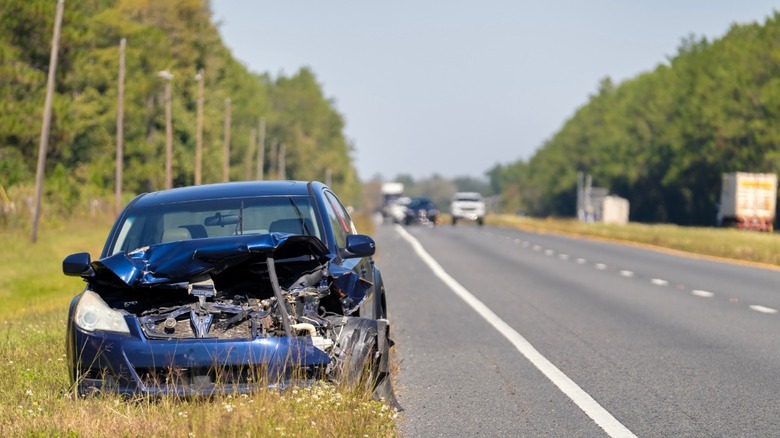 A heavily damaged blue car by the side of the highway