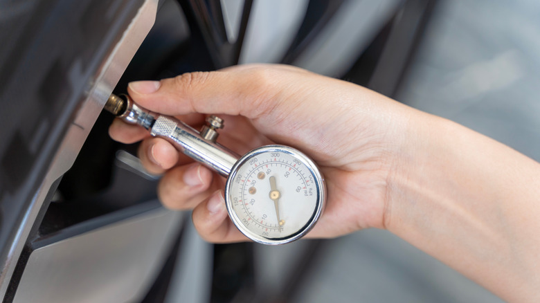 A hand holds a mechanical gauge to check tire pressure