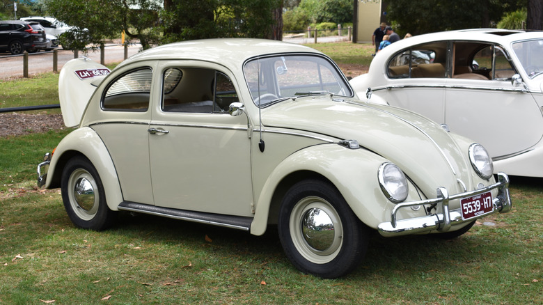 An off-white 1965 Volkswagen Beetle at a car show