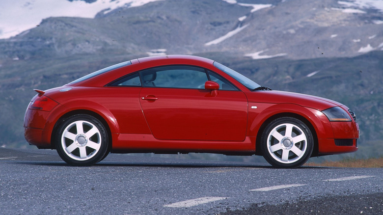 A red first-generation Audi TT Coupe parked on a road by the mountainside