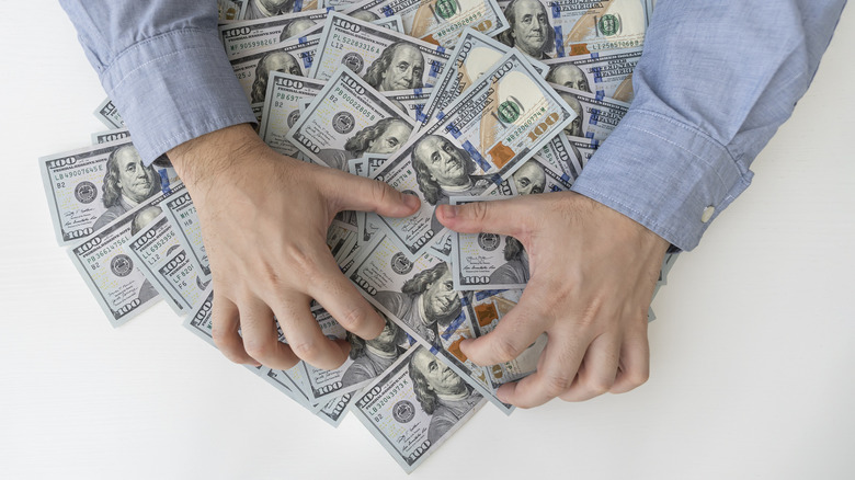 Close up of hands grabbing $100 bills.