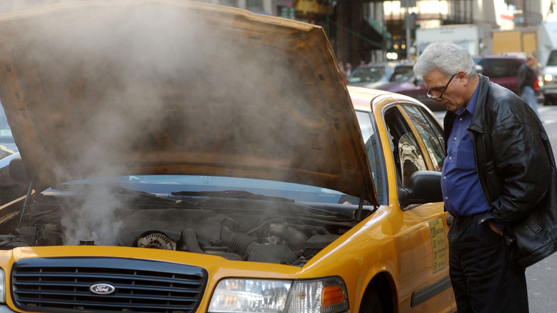 A taxi driver looks at his overheating engine