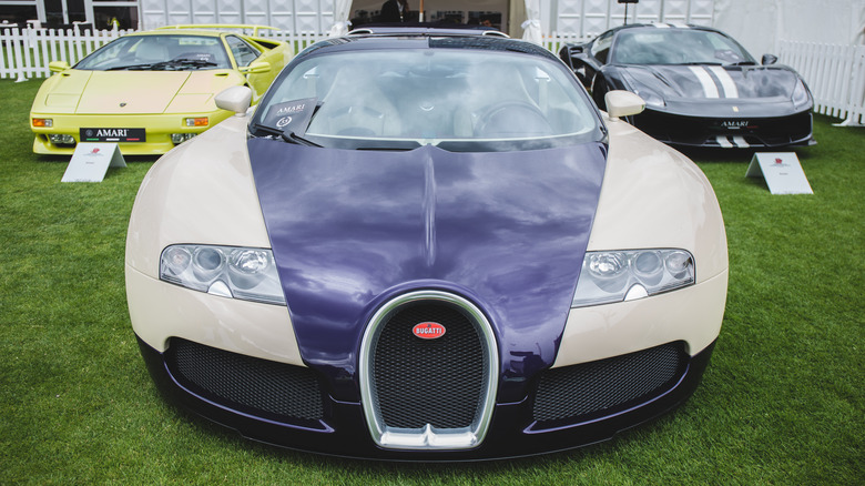 An outdoor concours display of a two-tone Bugatti Veyron sandwiched by a yellow Lamborghini Diablo and a gray Ferrari 488 Pista.