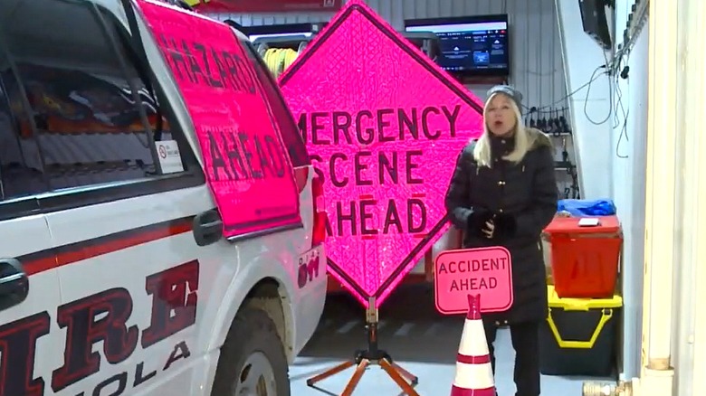 A female news reporter standing by pink traffic signs