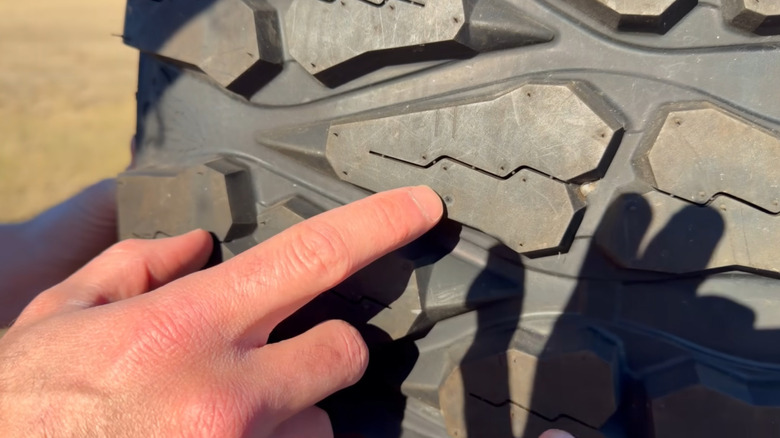 A person's finger pointing at a mark on a tire made by a bullet