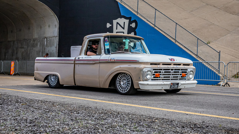 A vintage Ford F100 pickup with lowered suspension cruising on a side street