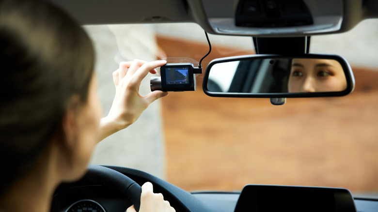 A woman inspects her dashcam while seated in her car