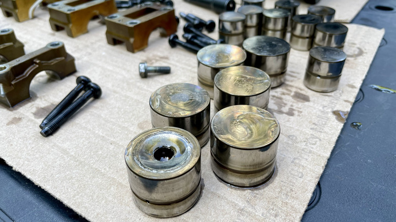 Hydraulic lifters on a workbench, with a damaged one sitting in the foreground.