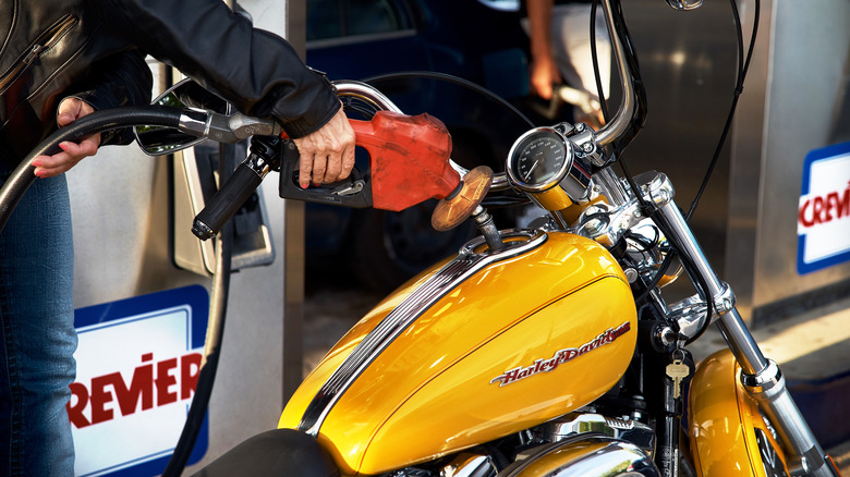 A hand filling the gas tank of a Harley-Davidson motorcycle at a gas station.