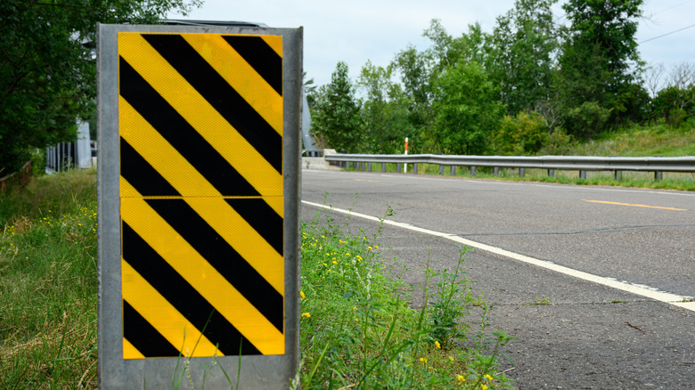 A black and yellow diagonal stripe sign next to a road.