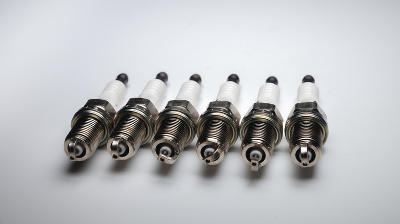 Six new spark plugs laid neatly amidst a grayish backdrop