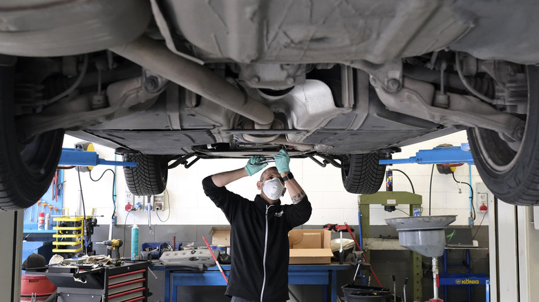 An auto mechanic standing under a car