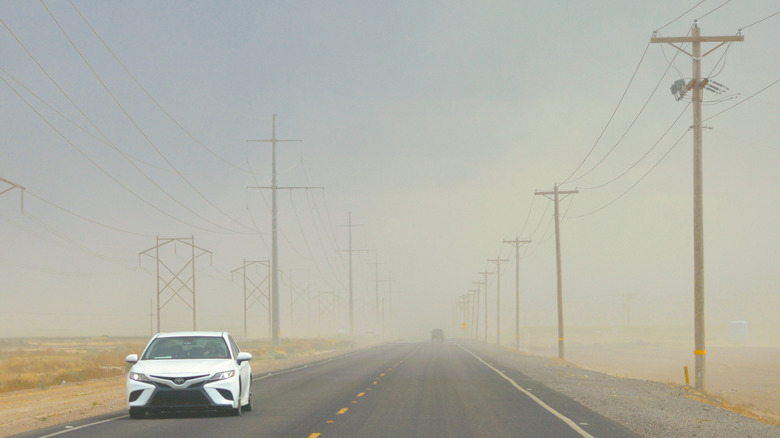 A car drives through a thick haze in the desert.