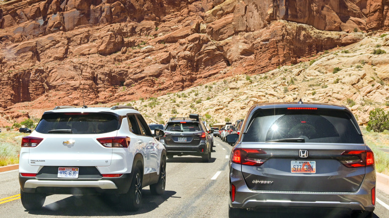 Cars drive through cliffs with reddish rocks.