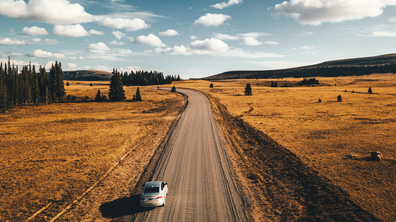 A single car drives on a long, empty road.