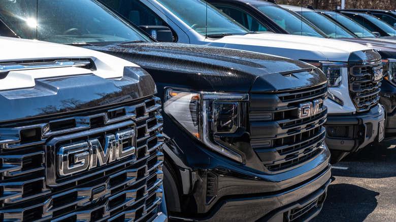 A line of GMC pickup trucks for sale at a dealership on a sunny spring day