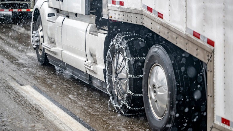 A semi truck with tire chains installed on a slick road in winter