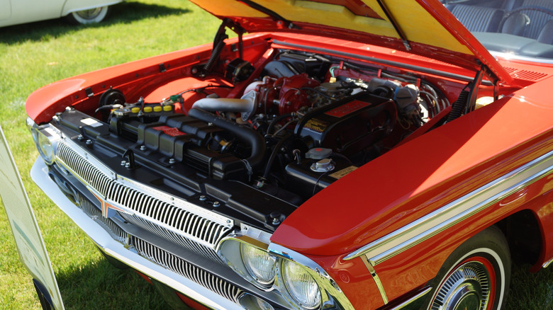 A red 1962 Oldsmobile Jetfire parked on grass at a car show