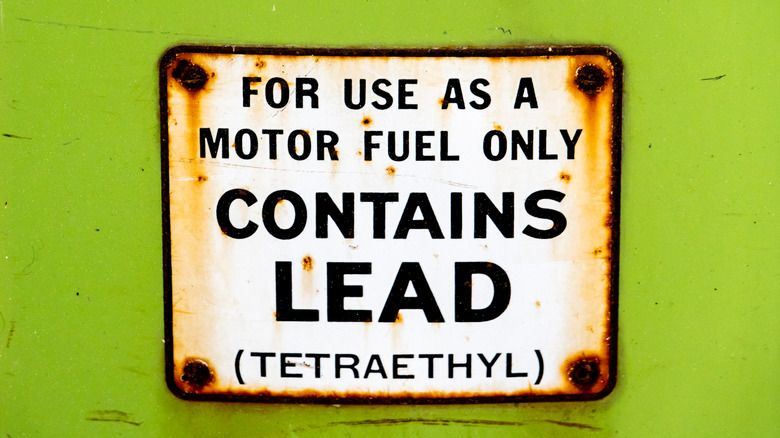 An old sign warning about lead in gasoline, mounted on a lime green wall