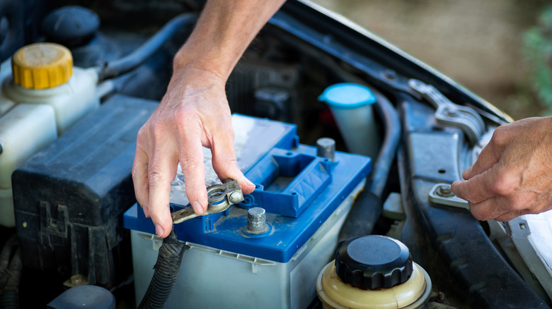 A person connects a car battery's lead under the hood of a car.