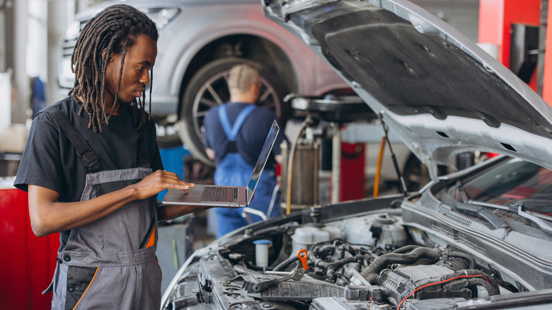 A mechanic using a laptop and software to diagnose and repair a car in a workshop