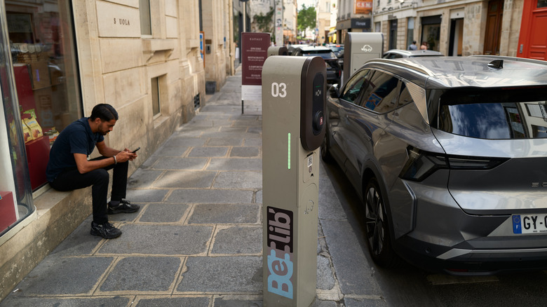 PARIS, FRANCE - AUGUST 5: A man checks his phone next to an electric vehicle charging at a station on August 5, 2026 in Paris, France. (Photo by Pierre Crom/Getty Images)