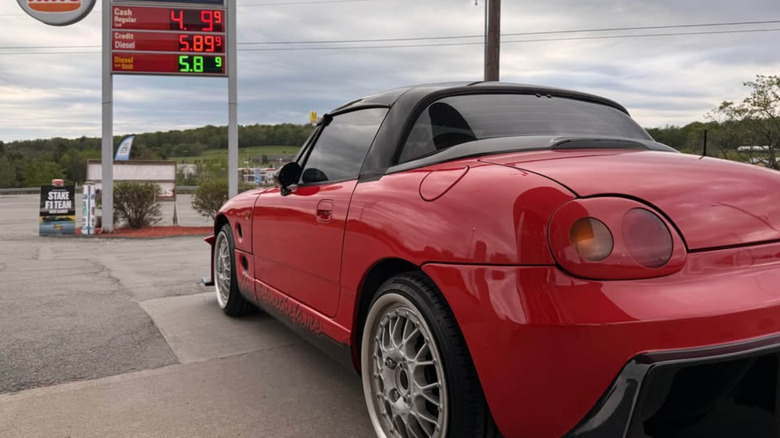 Red Suzuki Cappucino from the rear in front of fuel signs