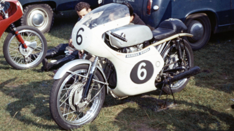 A 1960s silver Honda CR93, with white racing Hannah Honda fairing, parked on grass.