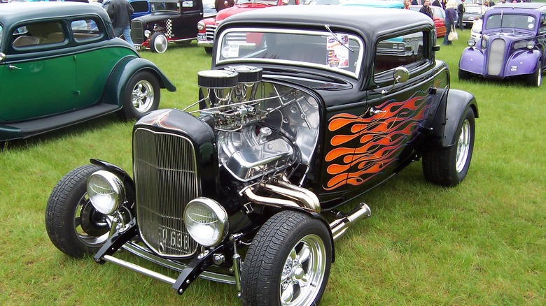 Black  and flame-painted Highboy-style 1932 Ford Deuce Coupe hot rod, seen from left front three-quarter view parked at an outdoor car show