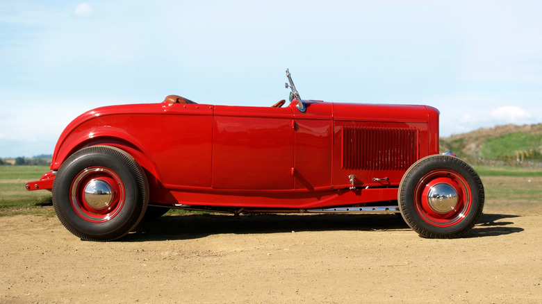 Side view of a red 1932 Ford Roadster hot rod parked outside.