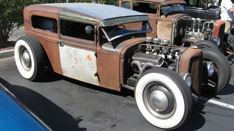 Rusty brown rat rod station wagon with exposed engine and no fenders, seen from right front three-quarter view