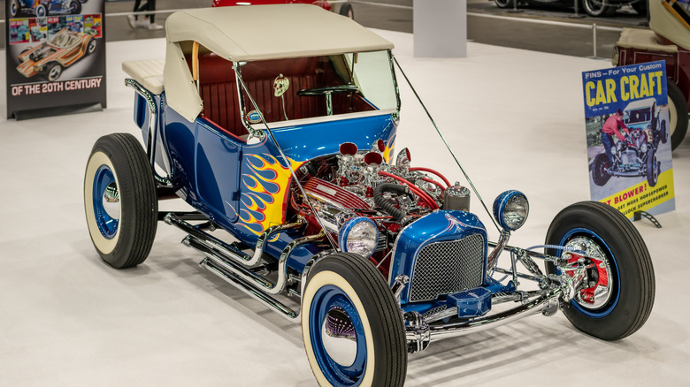 Blue T-bucket roadster known as Kookie T seeb=n from right front three-quarter view display expoed engine, chrome side pipes, and flame paint job
