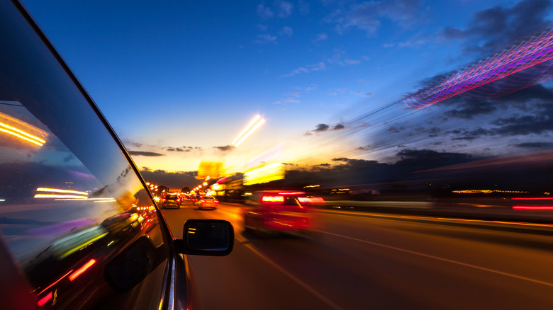 A car drives on a motorway in the dark with blurring lights of cars passing.
