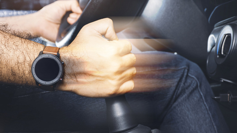 A hand on a car stick shift, blurred as the driver quickly works through the gears.