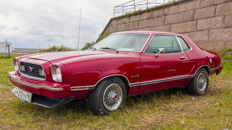 A red vintage Ford Mustang ii parked on a lawn.