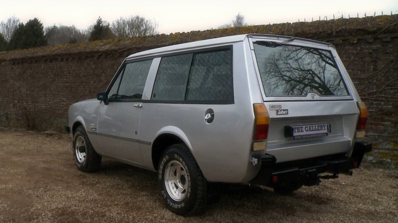 A silver Monteverdi Safari parked in front of a brick wall.