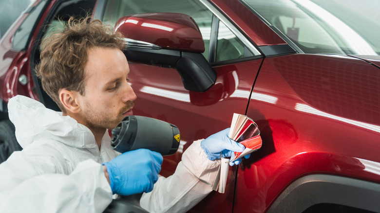 An automotive painter compares paint chips to the vehicle in the paint booth, using a color-match lamp.