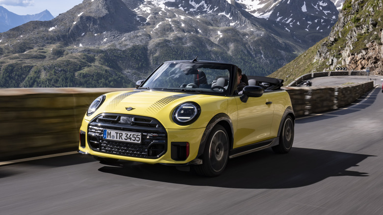 A yellow Mini JCW Convertible driving down a road with the top down.