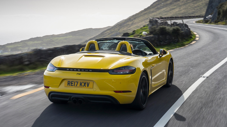 A yellow Porsche 718 Boxster S driving down a cliffside road with the top down.