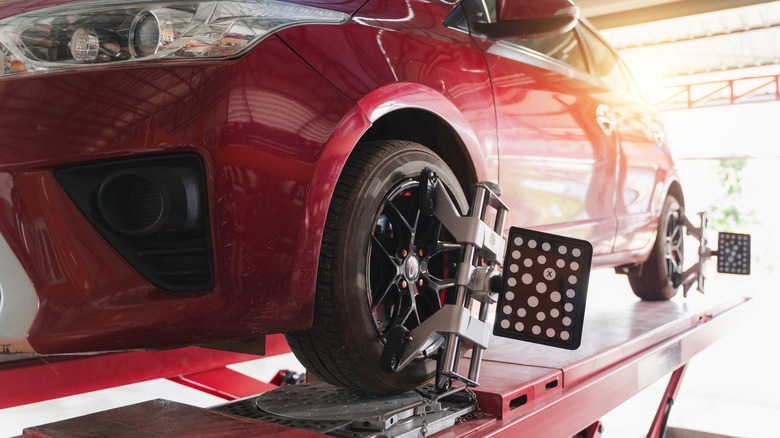 A red sedan sits atop an alignment rack with equipment hooked up to its wheels.